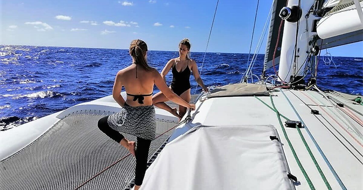 Two female crew members practicing yoga balance poses on the trampoline nets of the Rapido 60 trimaran Ineffable at sea.
