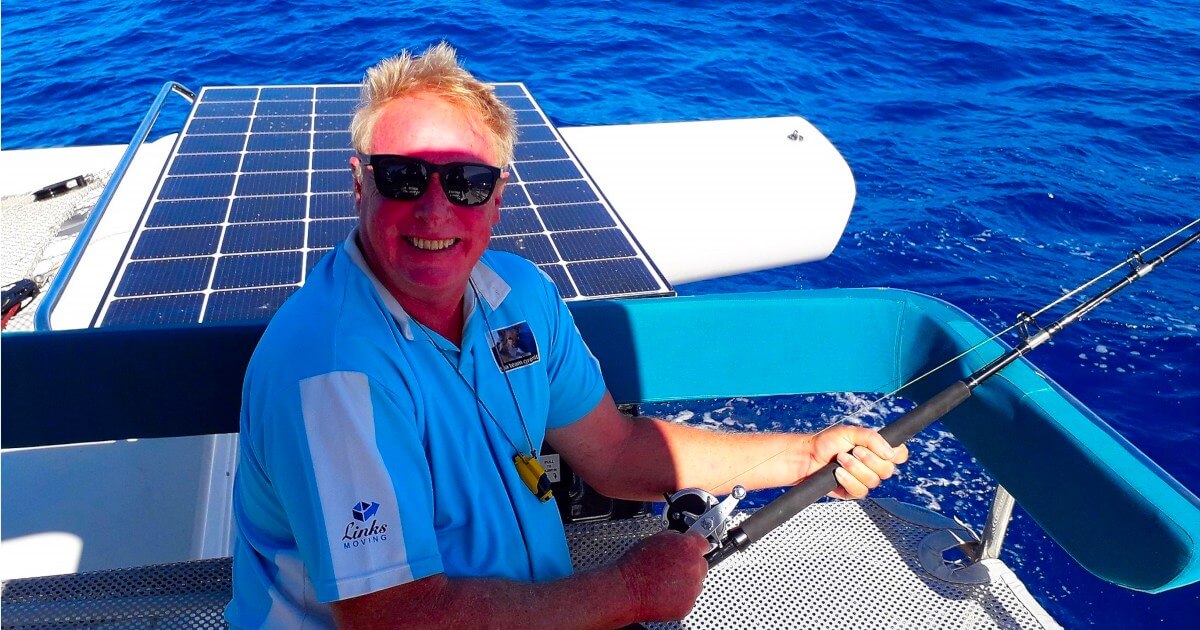 Steve Bourne holding a fishing rod on the deck of the Rapido 60 trimaran Ineffable at sea.