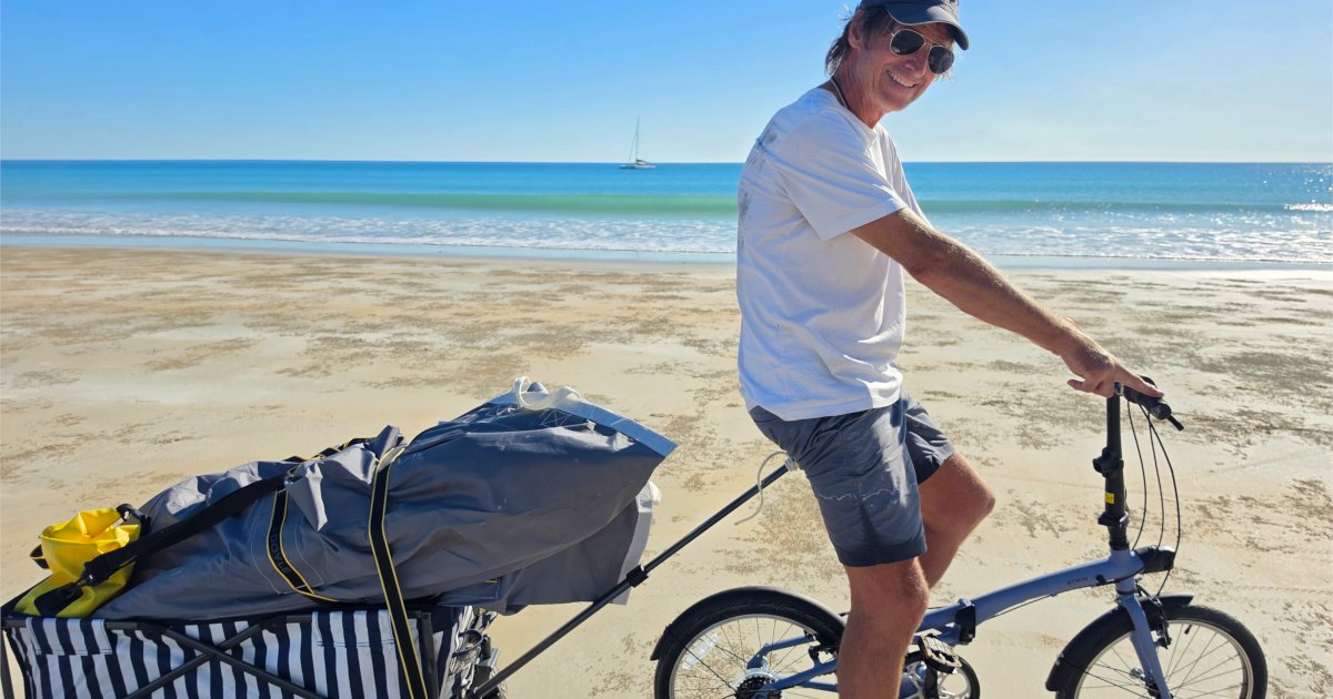 Alan Noble, owner of Rapido 40 Lightning, cycling along Cable Beach in Broome with a sail loaded onto a beach wagon.