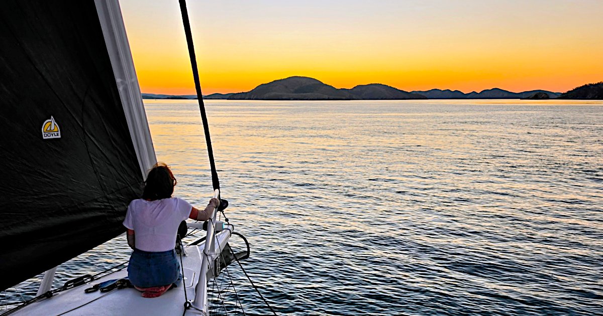 Woman sitting on the bow of Rapido 40 Lightning, looking towards a spectacular sunset over calm waters and distant islands.